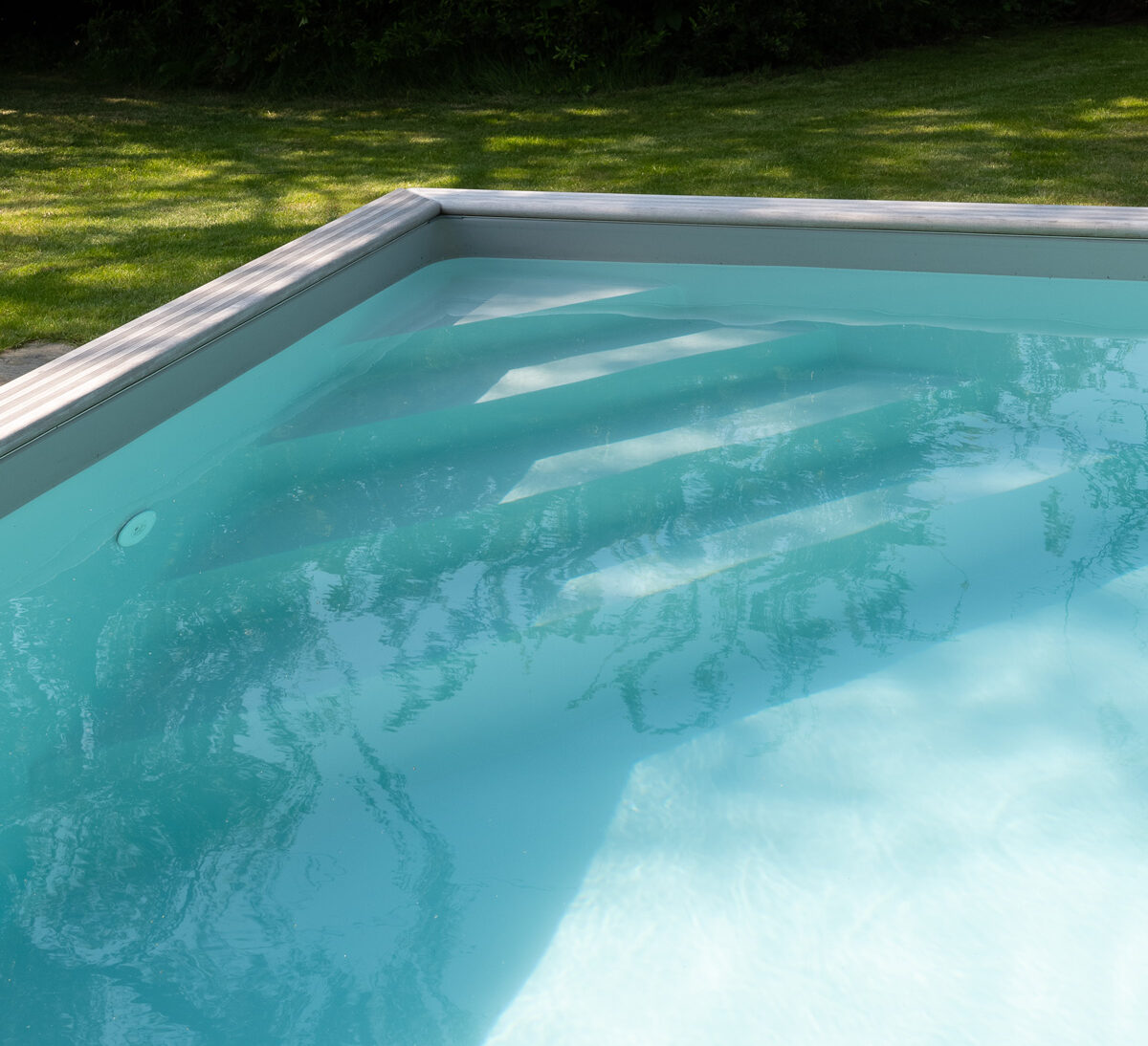 Detail van een houten zwembad met strakke liner, verstevigde afdekrand en rustige waterlijn in een groene tuin