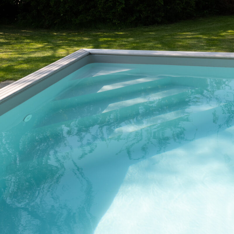 Detail van een houten zwembad met strakke liner, verstevigde afdekrand en rustige waterlijn in een groene tuin