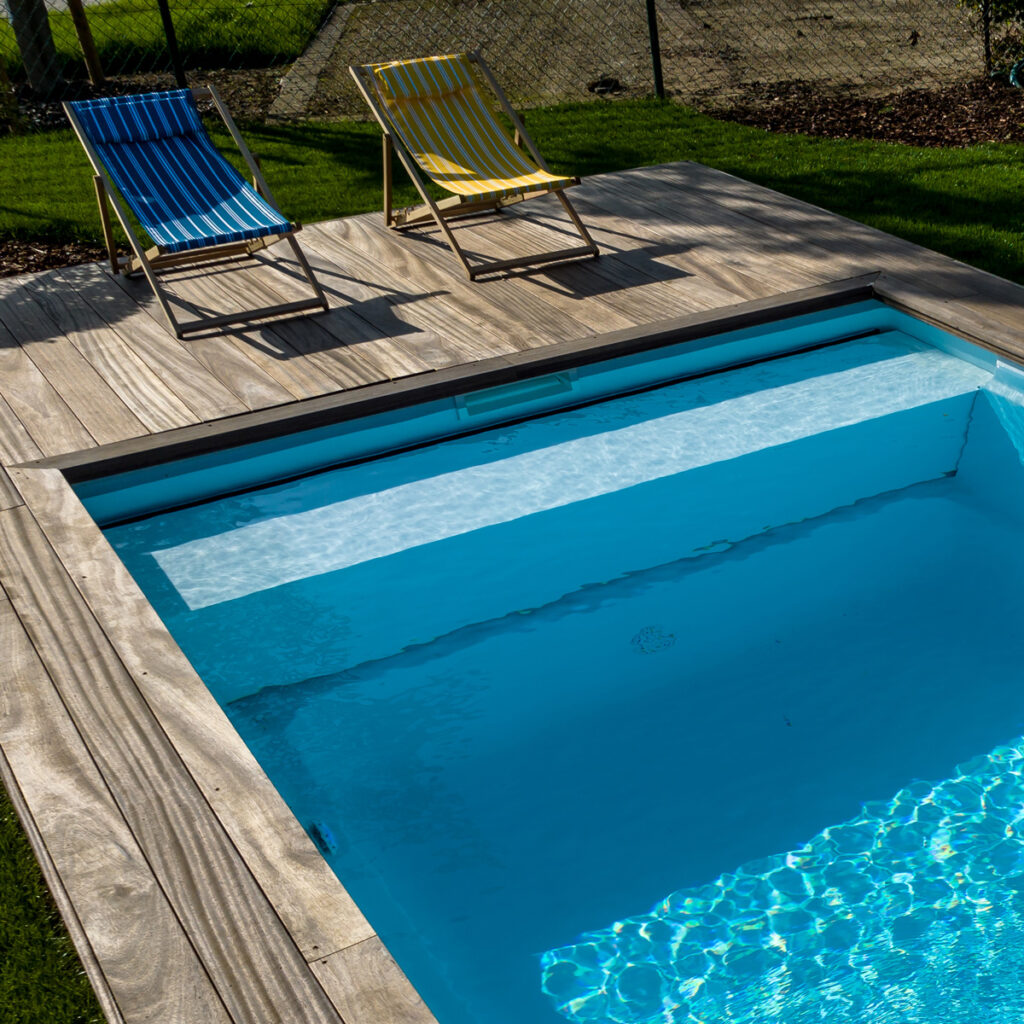 Vinylester monoblok zwembad met gladde, strakblauwe kuip naast een houten terras en ligstoelen