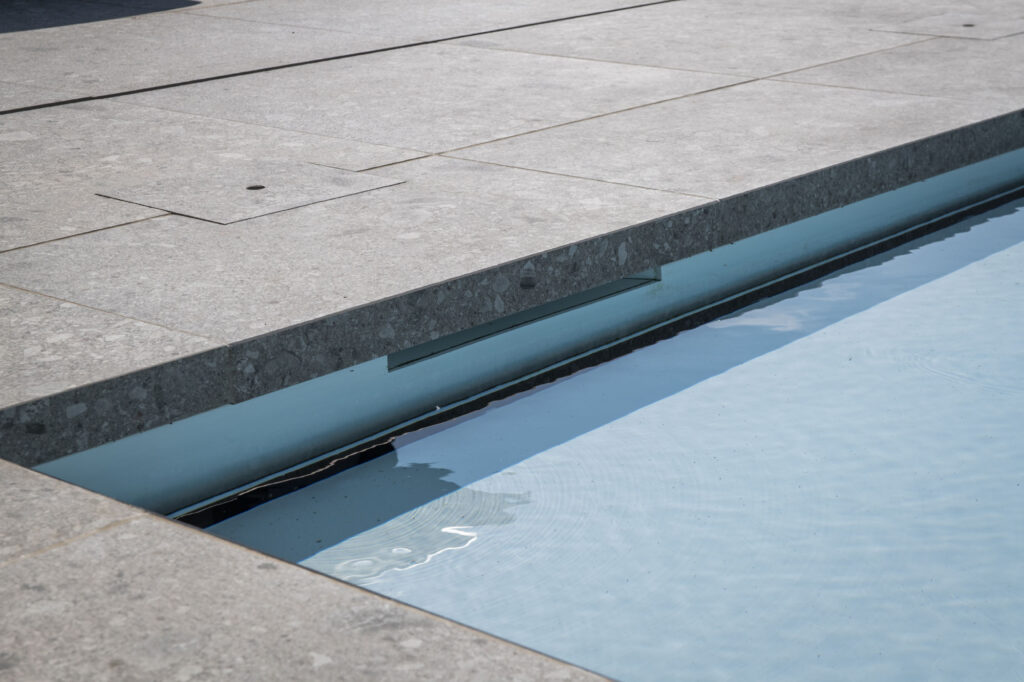 Detail van de skimmer en waterlijn van een ingebouwd zwembad met natuurstenen boordstenen.