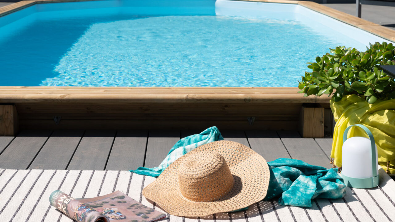 Houten zwembad klaar voor het zwemseizoen met zonnehoed en tijdschrift op het terras.