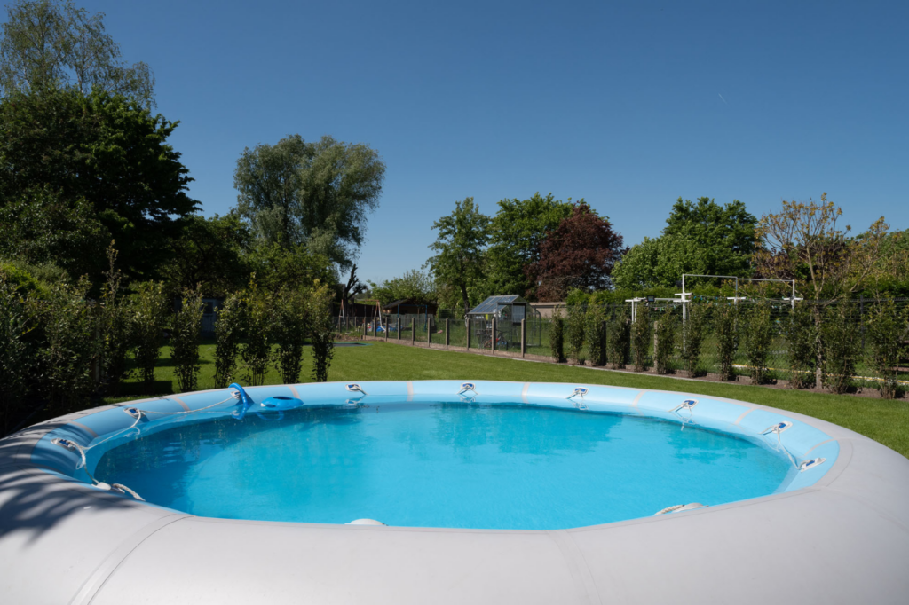 Rond Zodiac Original opbouwzwembad met lichtblauwe luchtrand, geplaatst op het gazon in een groene familietuin.