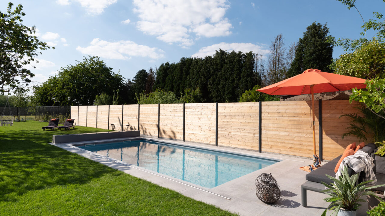 Ingegraven zwembad met houten schutting en zonnig terras.