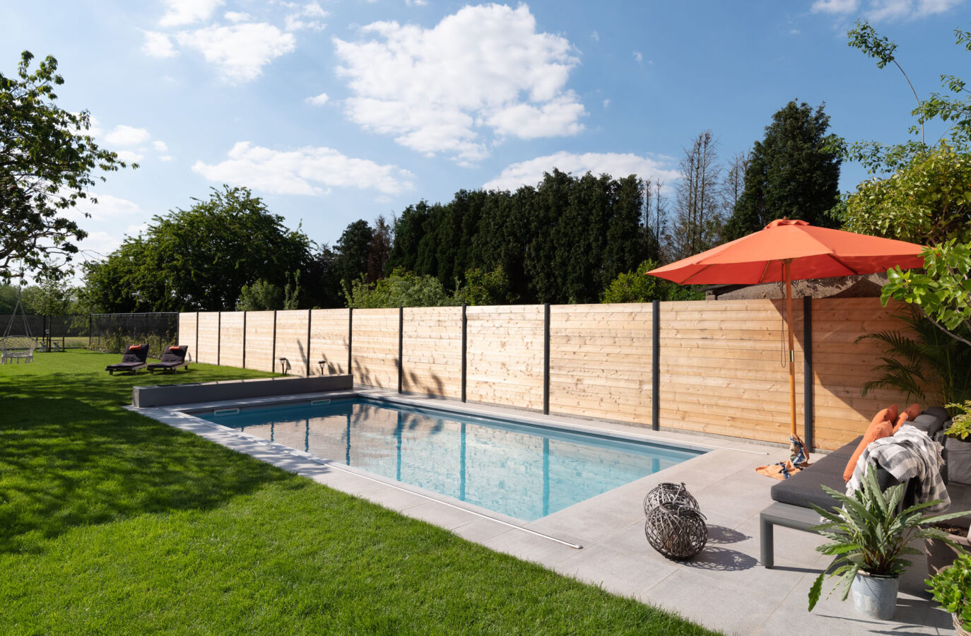 Ingegraven zwembad met houten schutting en zonnig terras.