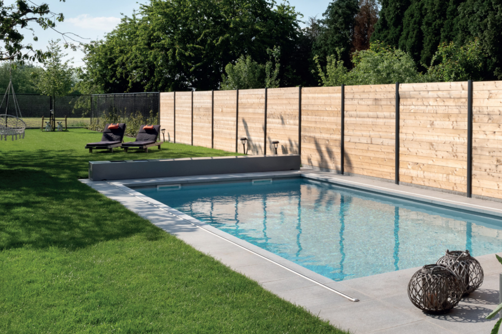 Bouwkundig zwembad met geïntegreerde zwembadrolluik langs een houten tuinafsluiting.